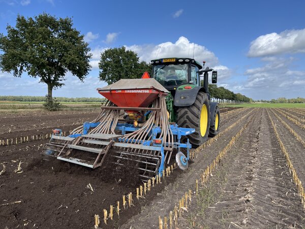 Een tractor met een aangebouwde zaaimachine op een akker na de maïsoogst.
